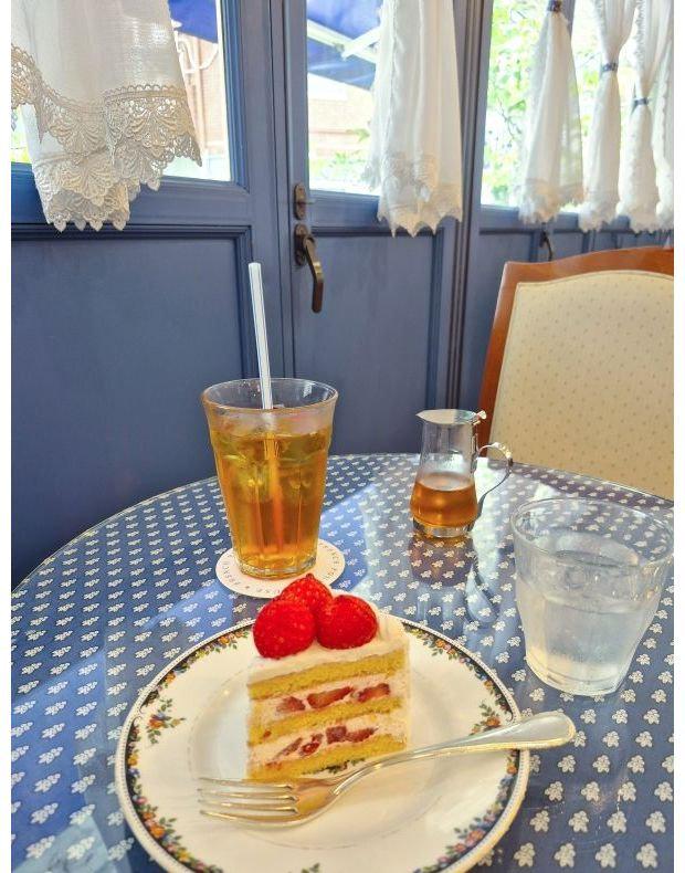 青いテーブルクロスに、ラズベリーをトッピングしたスライスケーキ、ティー、ウォーター、ピッチャーが並ぶカフェのテーブル