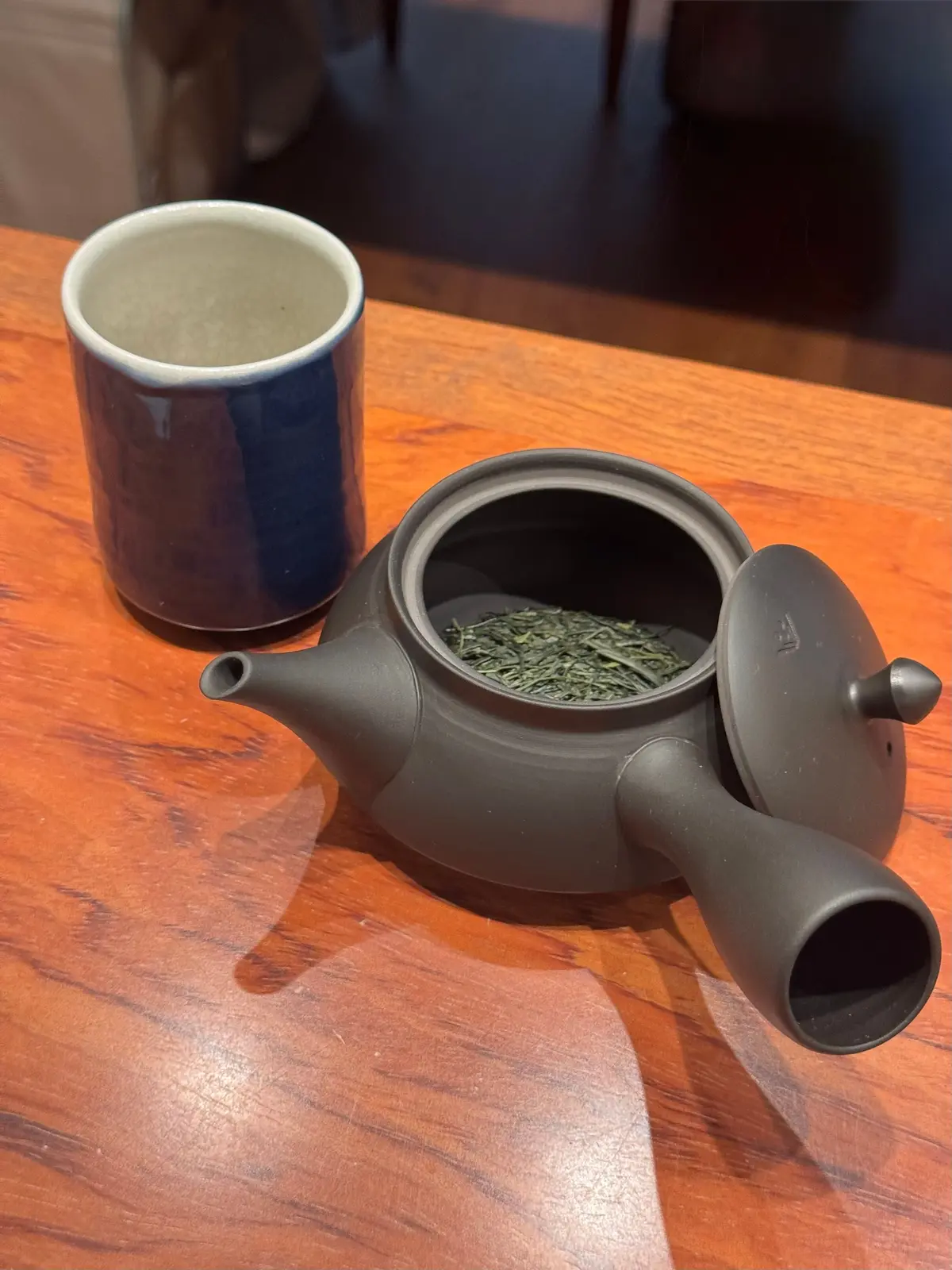 茶葉が入った黒いティーポットと青いマグカップが木製のテーブルに置かれている