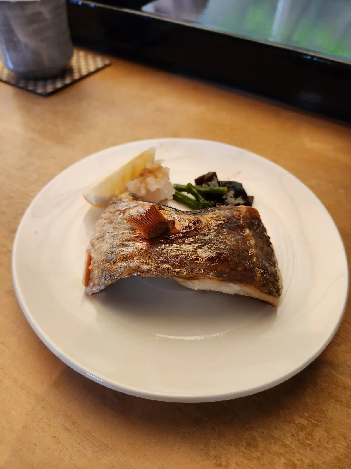 白い皿に焼き魚が盛り付けられ、レモン、玄米ご飯、グリーンピース、野菜が添えられている