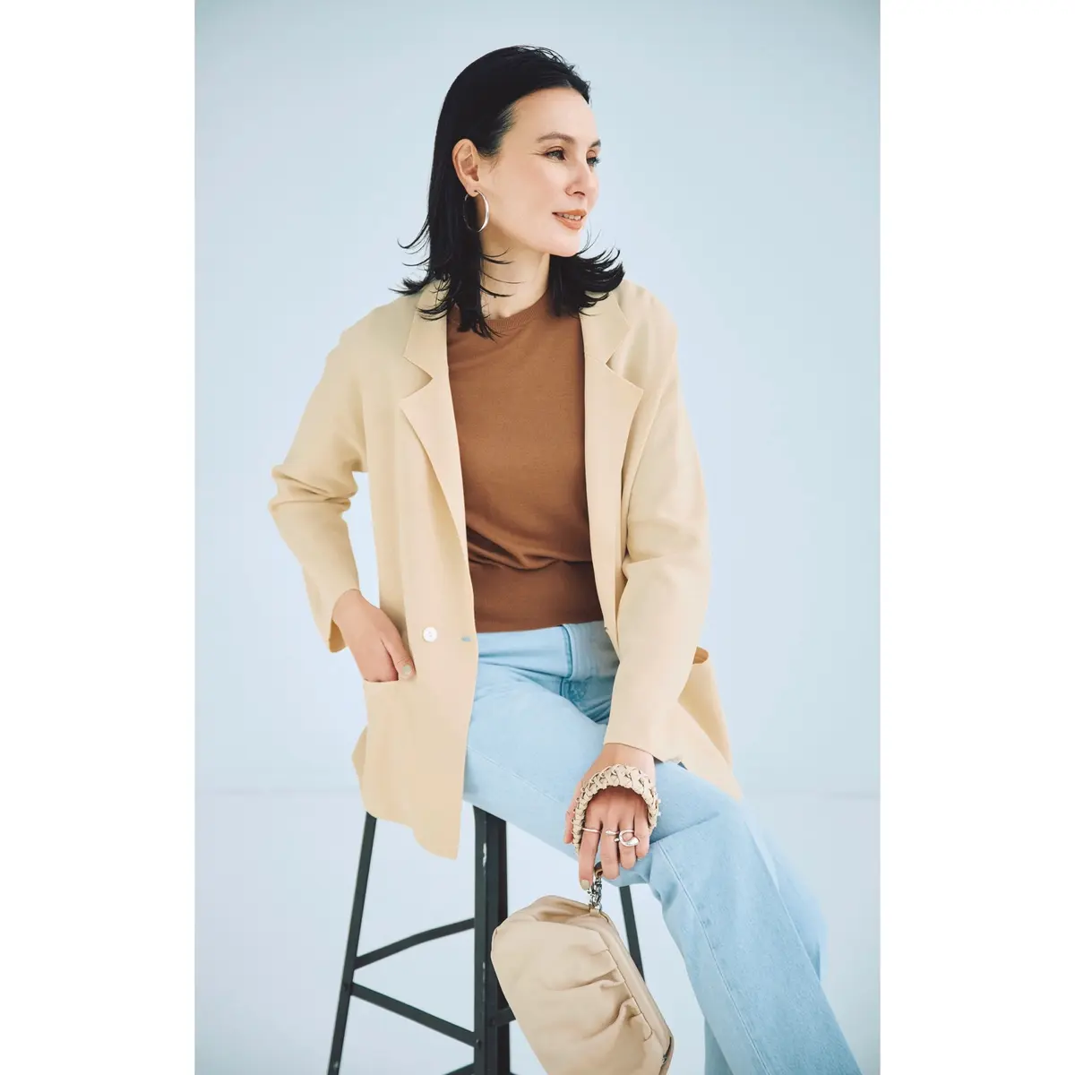 バニラ色のニットジャケットにブラウンTシャツ、ライトブルーデニムパンツを合わせたコーディネート　モデル・田沢美亜