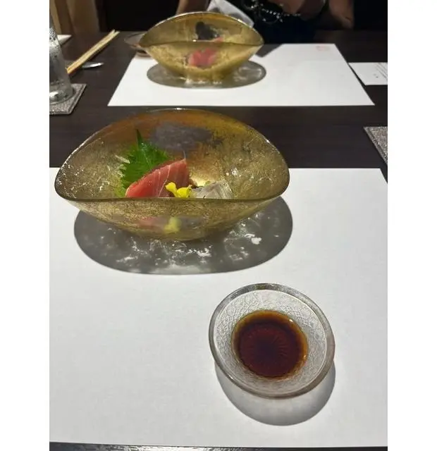 金色のガラス鉢に盛り付けられた刺身（マグロと白身魚）、添えられた薬味、そして醤油が小さなガラス鉢に入っている様子。