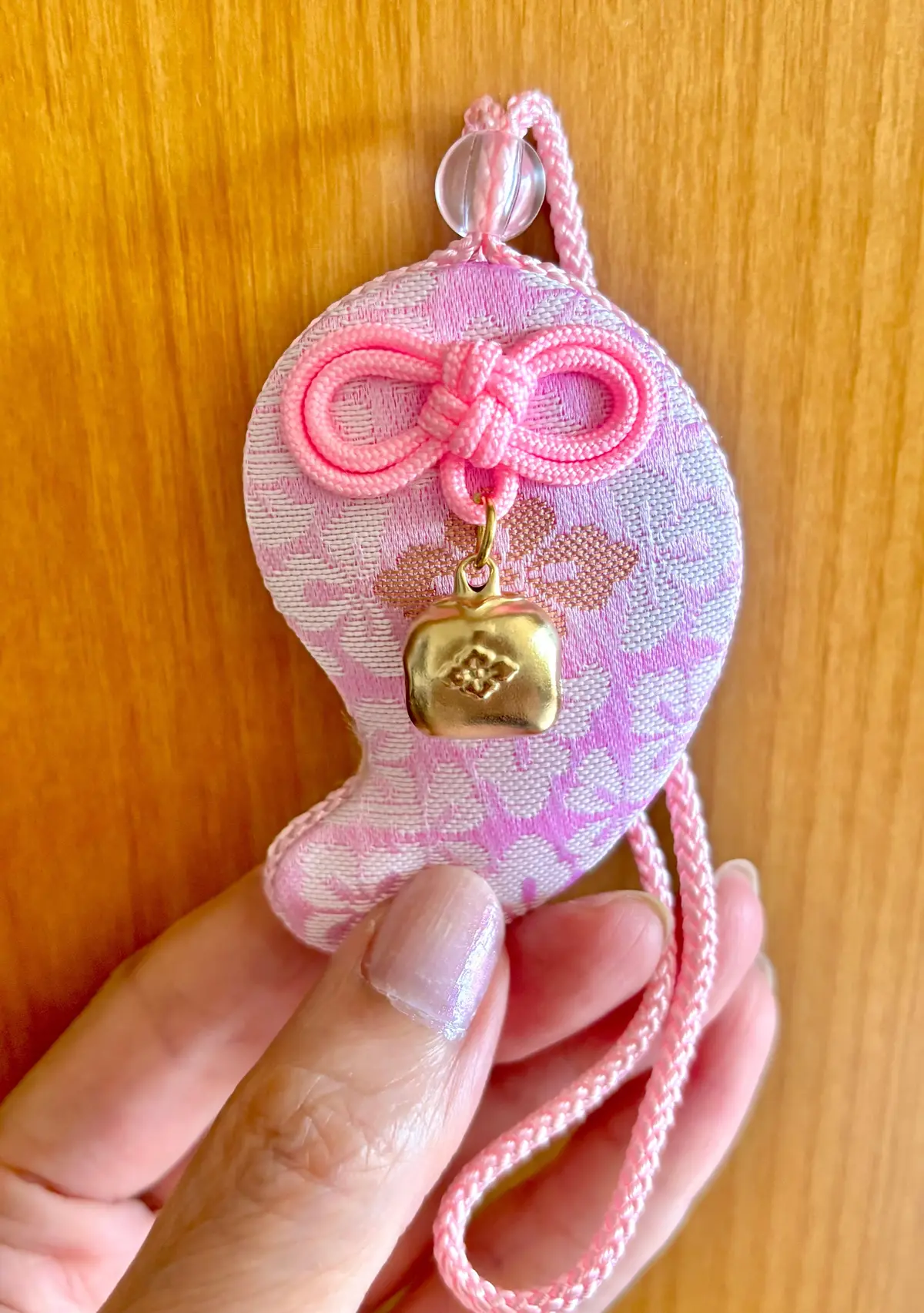 ピンクと白の桜柄の巾着に、金色の結び目の飾り。ピンクの紐で吊り下げられ、手で支えられている。