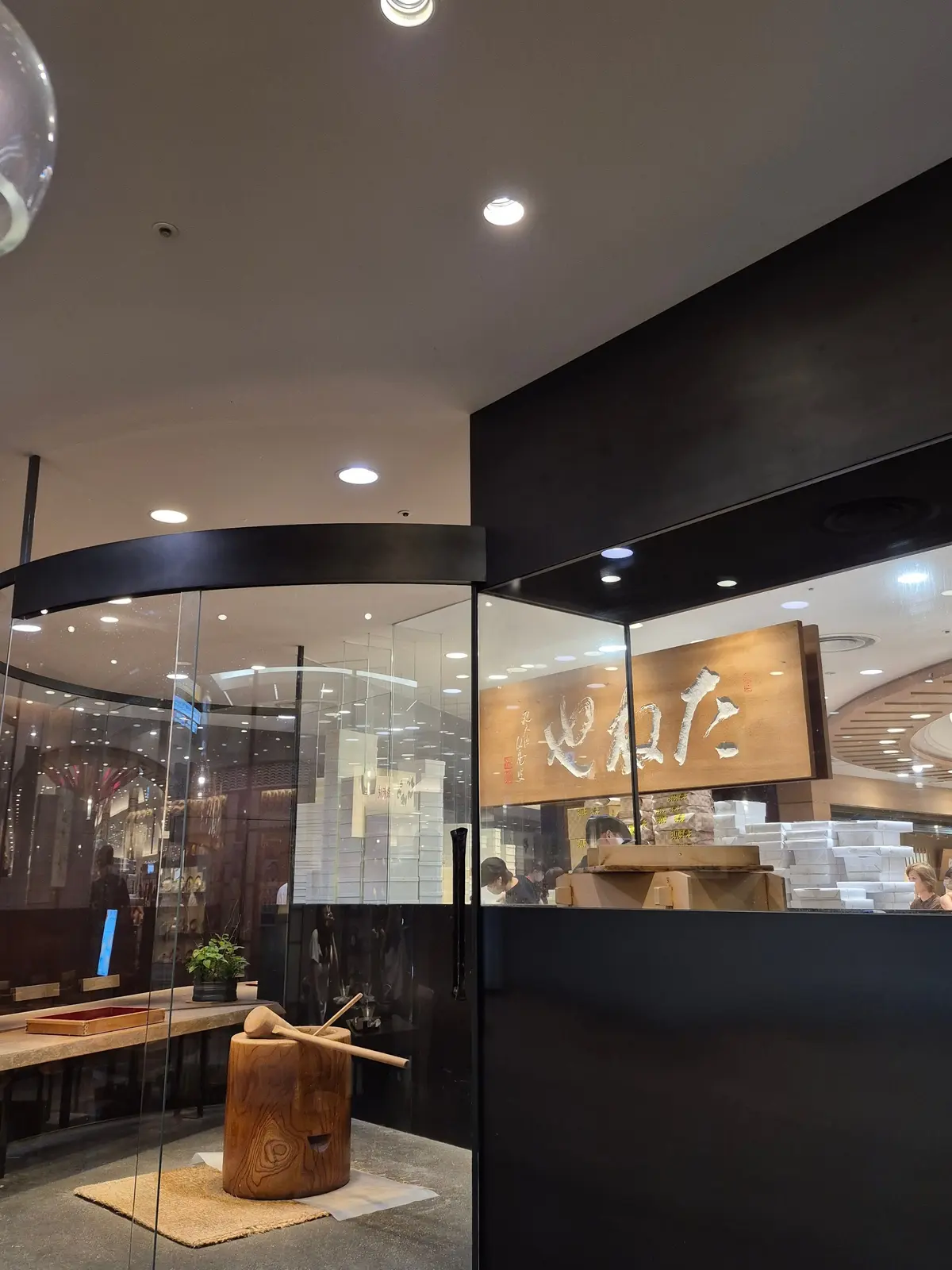 寿司店「築地金杉」の入り口。ガラス張りの店内にはカウンター席が見え、木製の大きな麺棒が置かれている。黒い柱に店名が書かれた木製の看板がある。