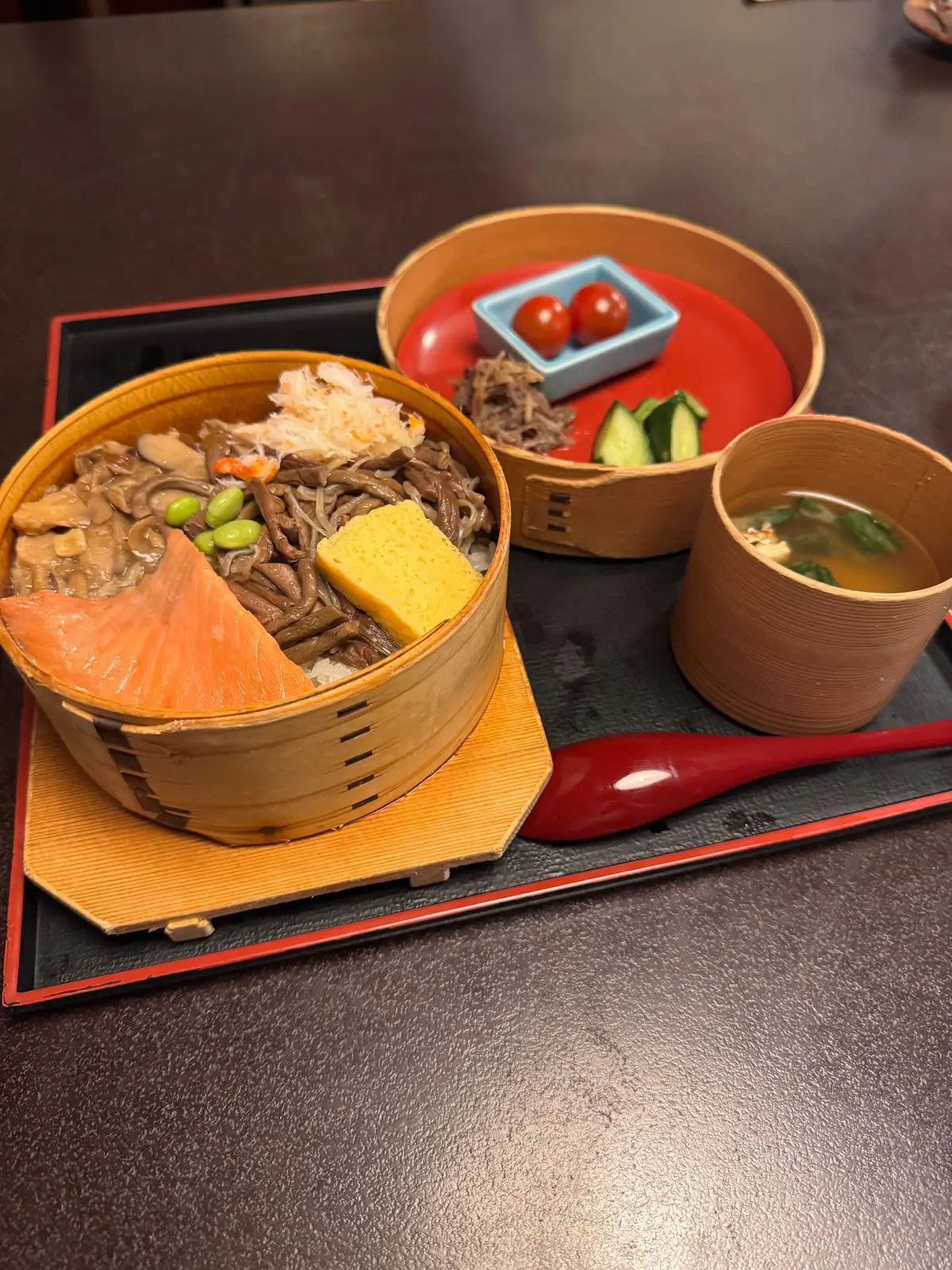 木製の丼にサーモン、豆腐、きのこ、わかめが盛り付けられた丼物と、トマト、きゅうり、わさびの小鉢、汁物が並ぶ料理セット