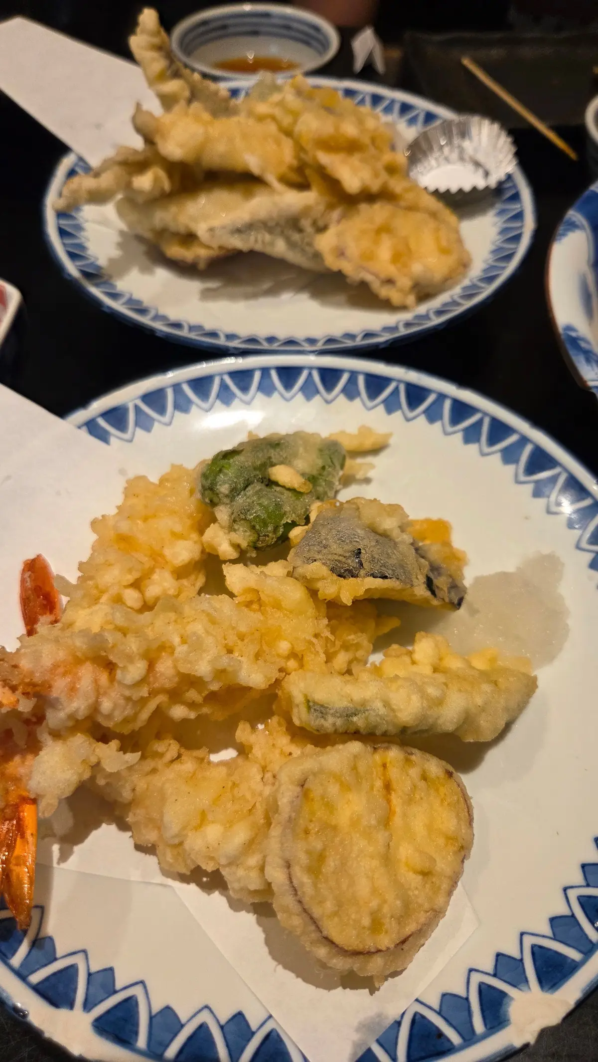 青い縁取りの皿に盛り付けられた天ぷら。エビ、野菜、キノコなどが、薄い衣で揚げられている。小皿と箸が添えられている。