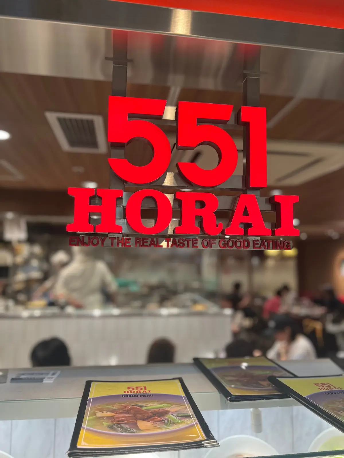 レストラン「551蓬莱」の入り口付近の様子。赤い数字の「551」と「HORAI」のロゴがガラス越しに見える。手前にメニューが置かれ、店内の様子がぼんやりと見える。