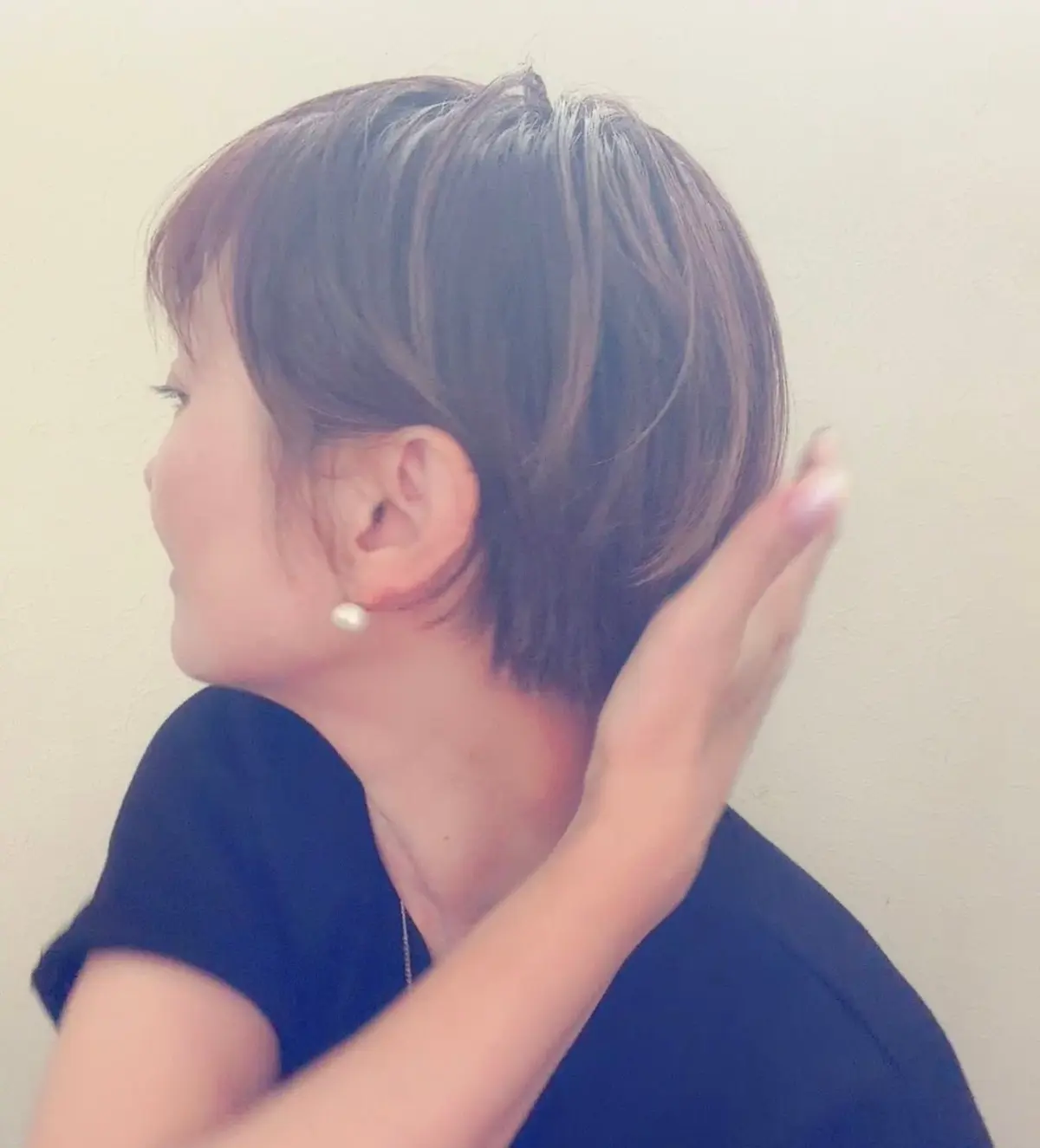 ショートカットの女性が左を向いており、真珠のイヤリングを着用しています。右手で耳を触れています。