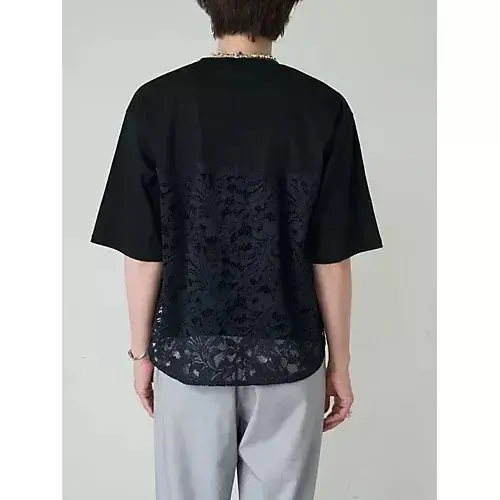 黒色のゆったりとしたTシャツを着用した男性の後ろ姿。Tシャツの上部は無地で、下部は黒のレース模様が施されている。灰色のパンツを履き、首にはチェーンのネックレスを着用。背景は無地。