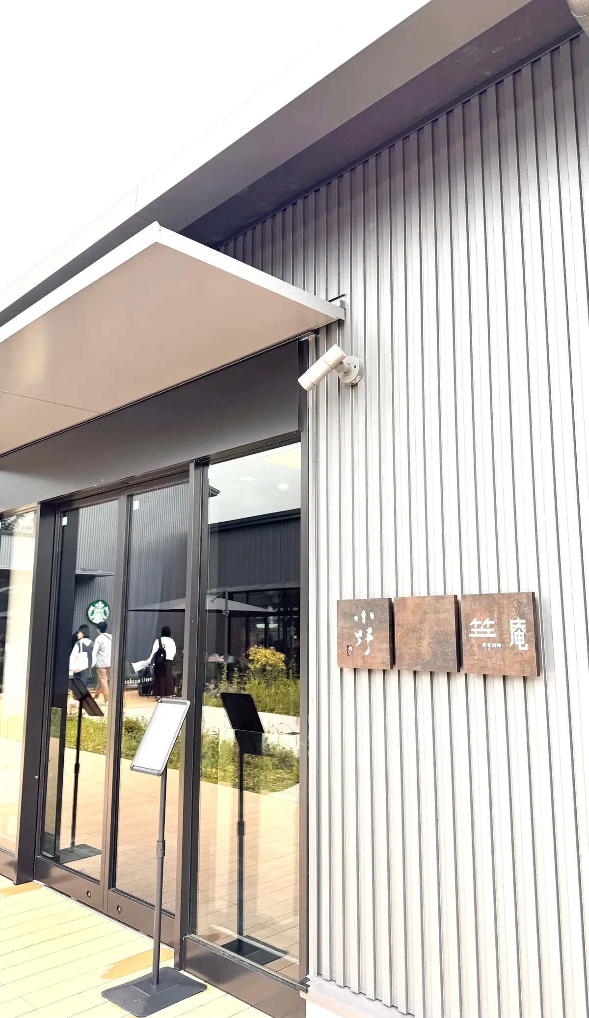 白い建物に設置されたガラス張りの入り口と、右側に木製の看板が設置されている外観。看板には漢字とひらがなで「経庵」と書かれている。