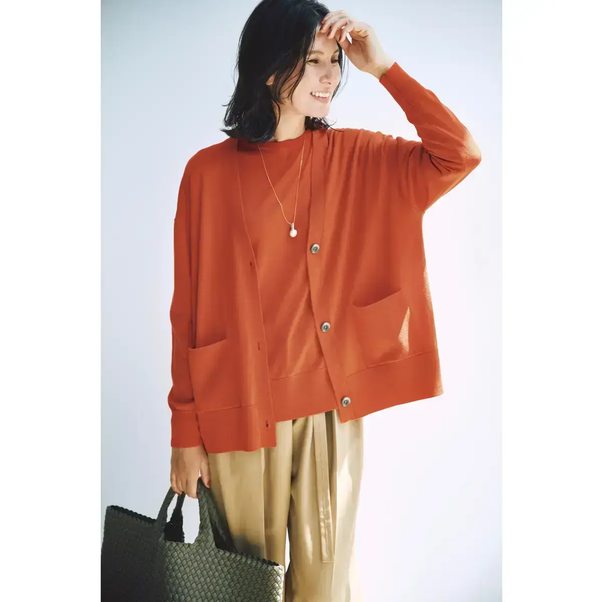 鮮やかなオレンジのアンサンブルニットは、まろやかなベージュパンツで上品に着こなす
