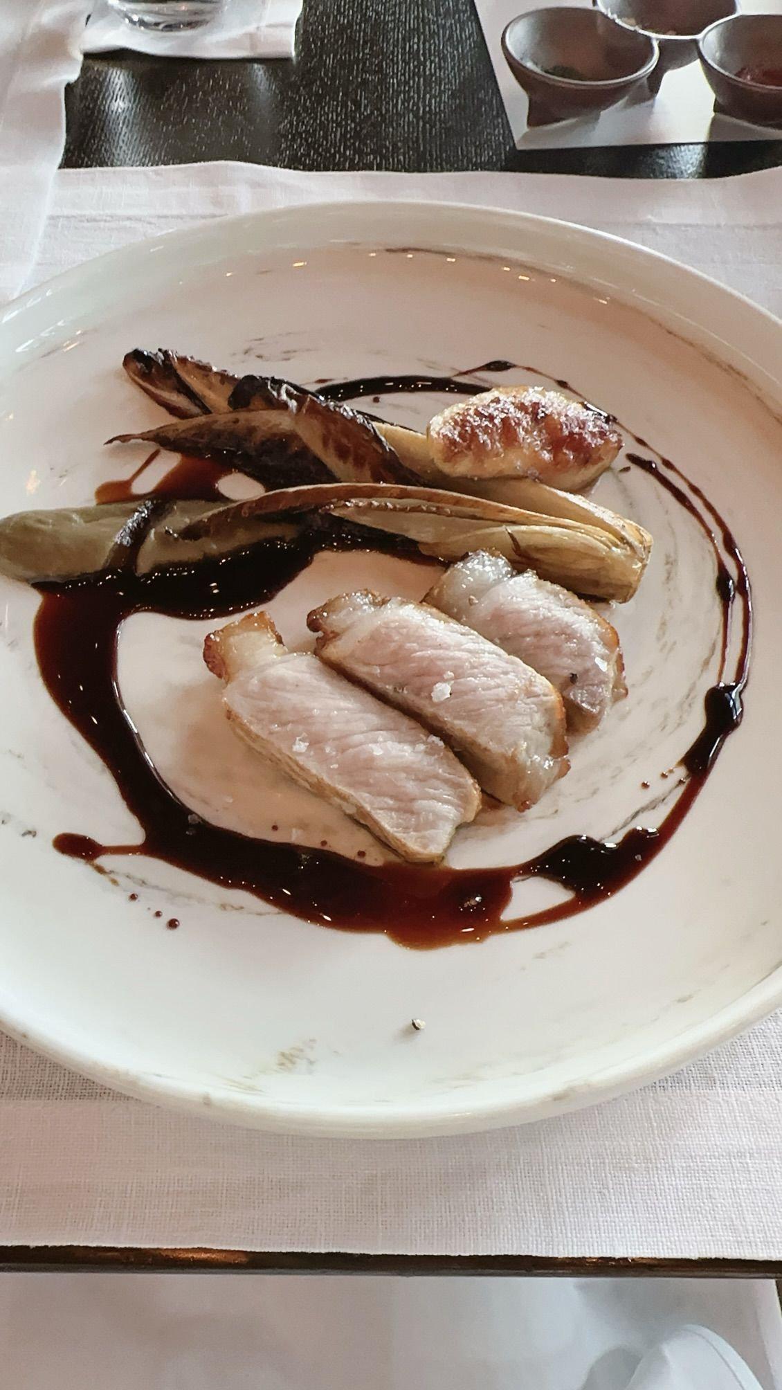 白い皿に、肉、野菜、ソースが盛り付けられた料理。肉は薄切りで、野菜は細長く、ソースは皿全体に波紋のように広がっている。