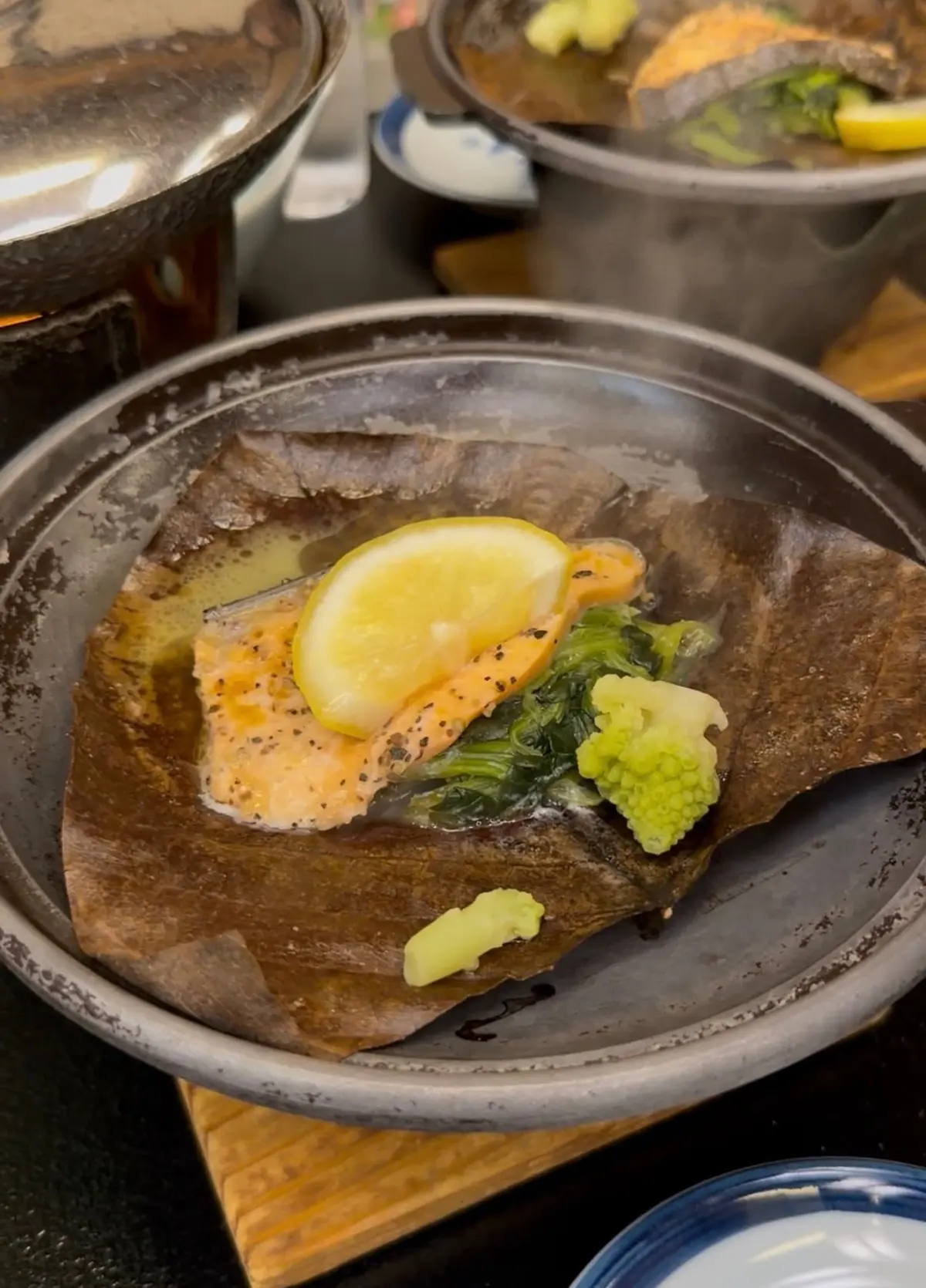鉄製の鍋に盛り付けられた、鮭のソテー。レモン、葉物野菜、ブロッコリーなどが添えられ、和風の出汁が注がれている。