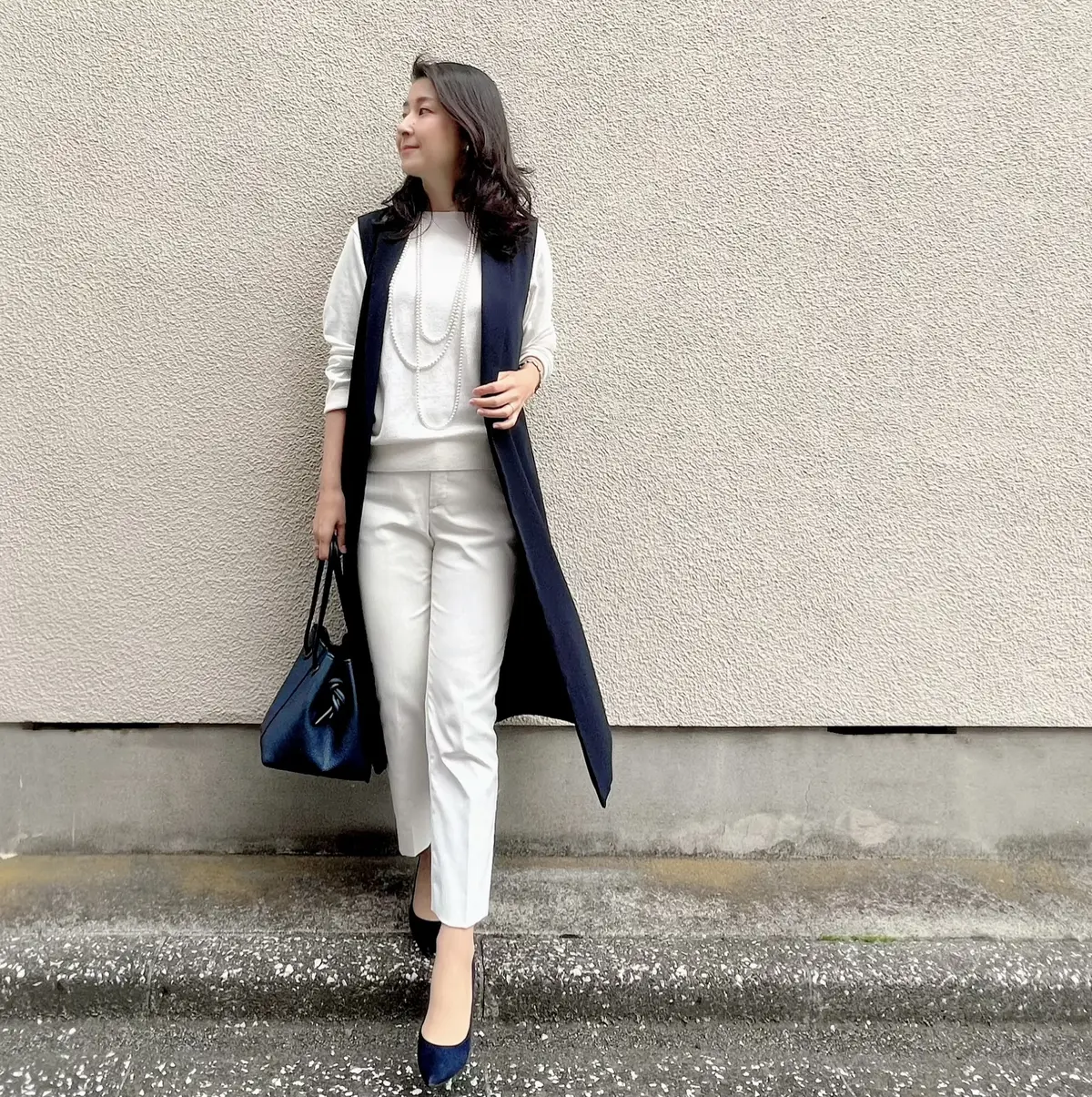 白ニット　白パンツ　ネイビーのロングジレ　ネイビーのバッグ　ネイビーのパンプス　パールの三連ロングネックレス