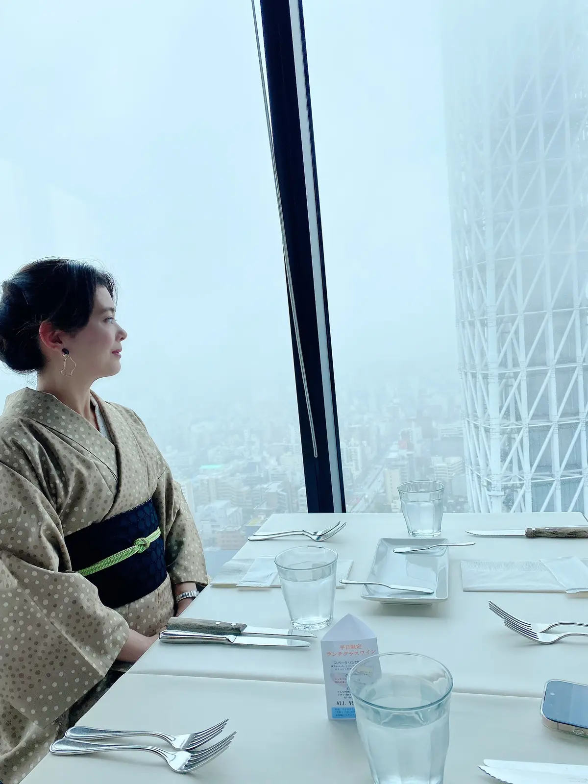 ブラッスリーオザミ東京スカイツリーソラマチ店のスカイツリーの見える窓際席に座る和服姿の女性の画像