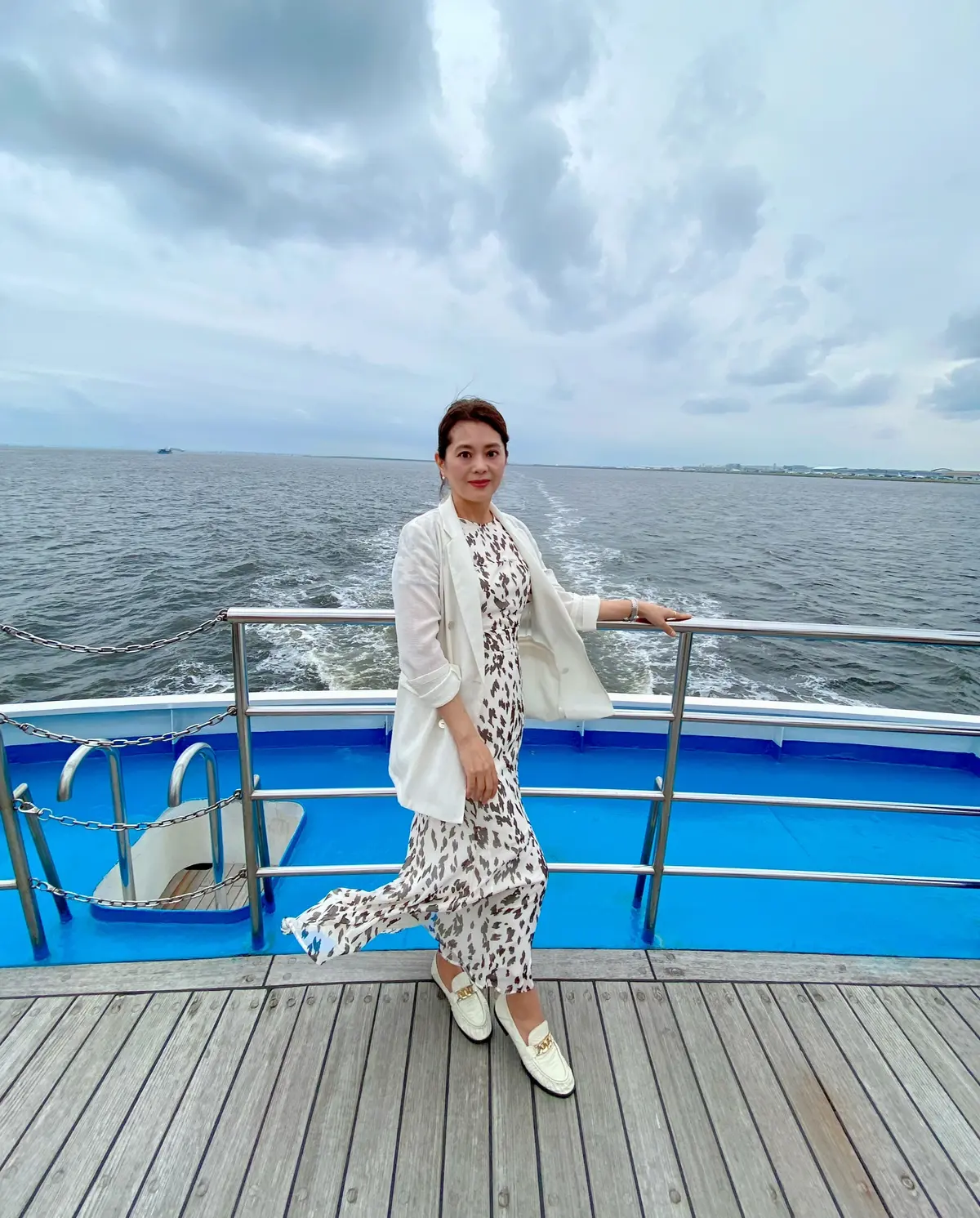 海を背景にした「レディクリスタル」のデッキで、風に揺れるシアージャケット、柄シフォンワンピースを着てトッズのローファーでと凛とした立ち姿の女性