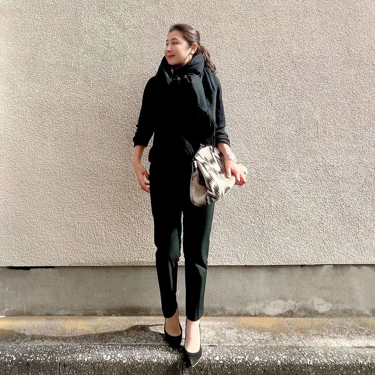 ユニクロ黒ニット、ユニクロ黒パンツ、黒パンプス、柄物のクラッチバッグ、黒の大判カシミヤストール