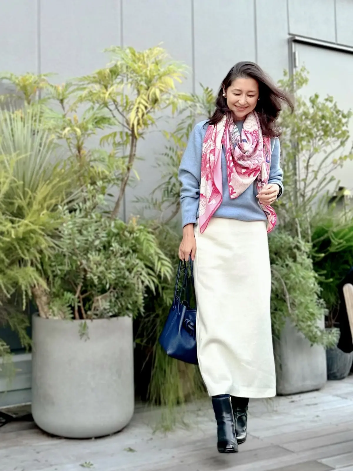 水色のニット、白のロングタイトスカート、ピンク系スカーフ柄大判ストール、ネイビーのショートブーツ、ネイビーのバッグ