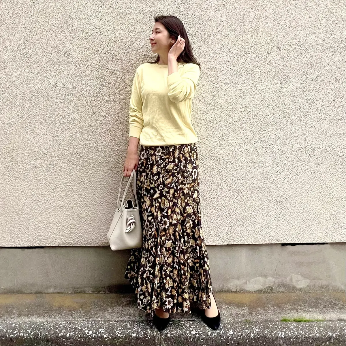 ユニクロのイエローニット、黒にイエロー系の花柄が描かれたロングスカート、オフホワイトのバッグ、黒のバンプス