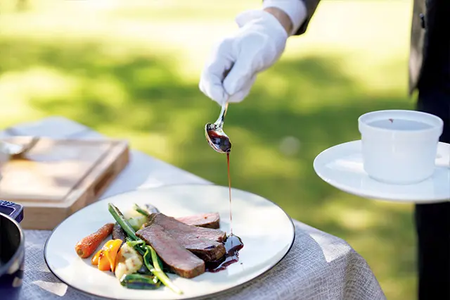 初夏から秋には庭にしつらえたクロ ス敷きのテーブルでサービススタッフがサーブ