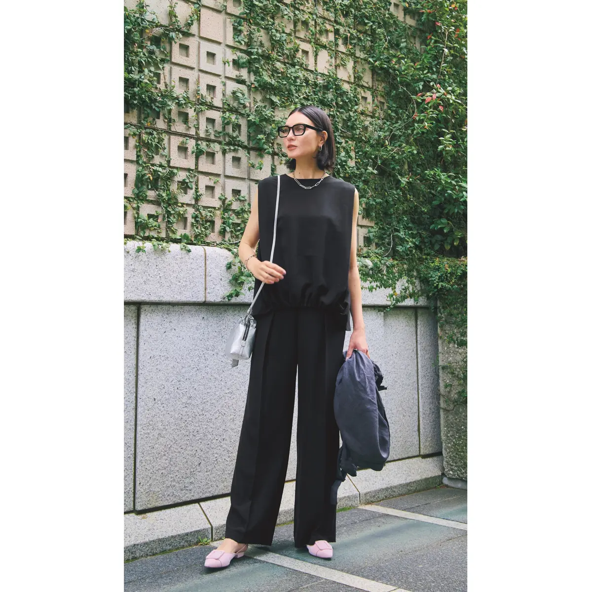 黒ノースリーブトップスに黒タックパンツを合わせ、足元に淡ピンクのミュールを添えたコーディネート　モデル・田沢美亜