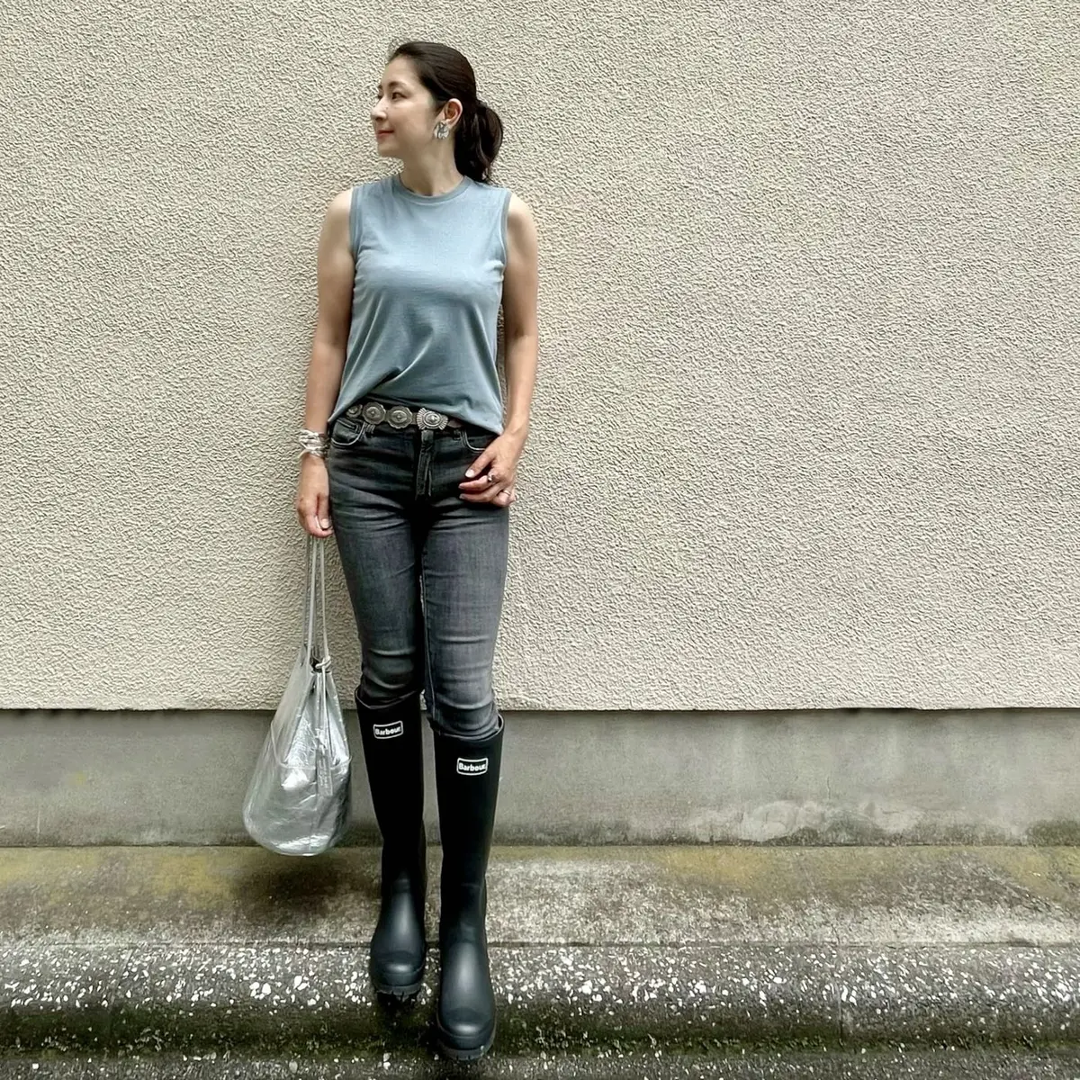 くるみブルーのノースリーブTシャツ、黒デニム、黒のレインブーツ、シルバーのバッグ、コンチョベルト