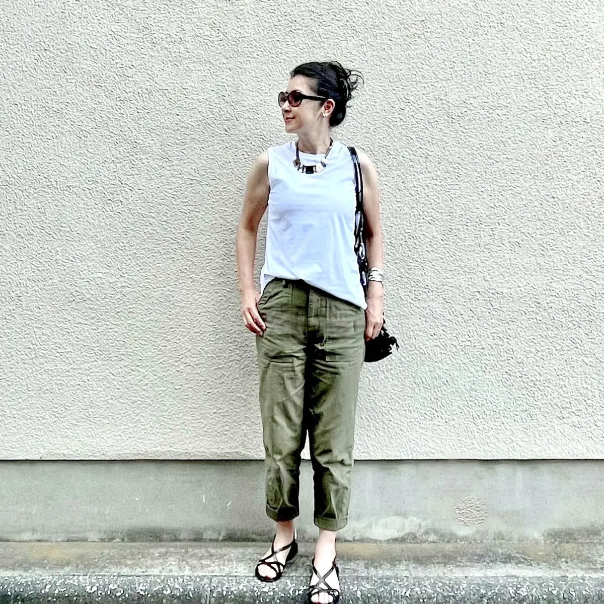 ユニクロの白のノースリーブTシャツ、カーキのベイカーパンツ、ブラックのフラットサンダル、ブラックのメッシュバッグ、大振りのショートネックレス