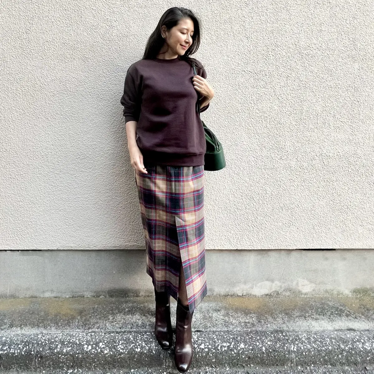 ブラウンのスウェットシャツ、ベージュ系のチェック柄タイトスカート、グリーンのバッグ、ブラウンのブーツ