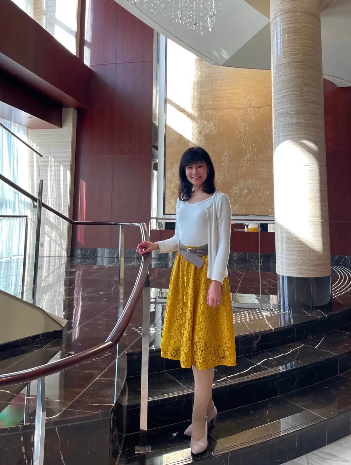 白ニットとからし色のレーススカート、太ベルトがアクセントのスカートコーデ。「シャングリラホテル」の螺旋階段