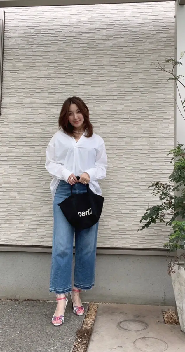 白い壁の前　ジーンズ、白シャツ、黒のトートバッグを持った女性