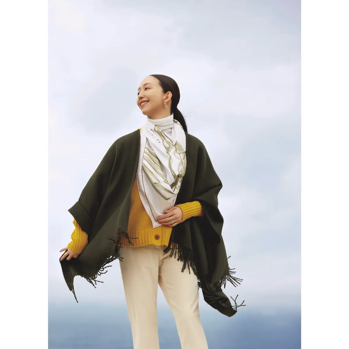 マスタードイエローのニットカーディガンとオフ白パンツを合わせ、カーキのローブを羽織り、首元に白スカーフを巻いたコーディネート　モデル・松島花　