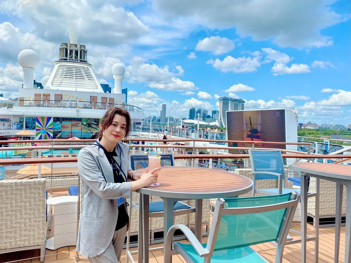 ロイヤルカリビアン社「アンセムオブザシーズ」のデッキでシンガポールスリングを片手に笑顔の50代の女性