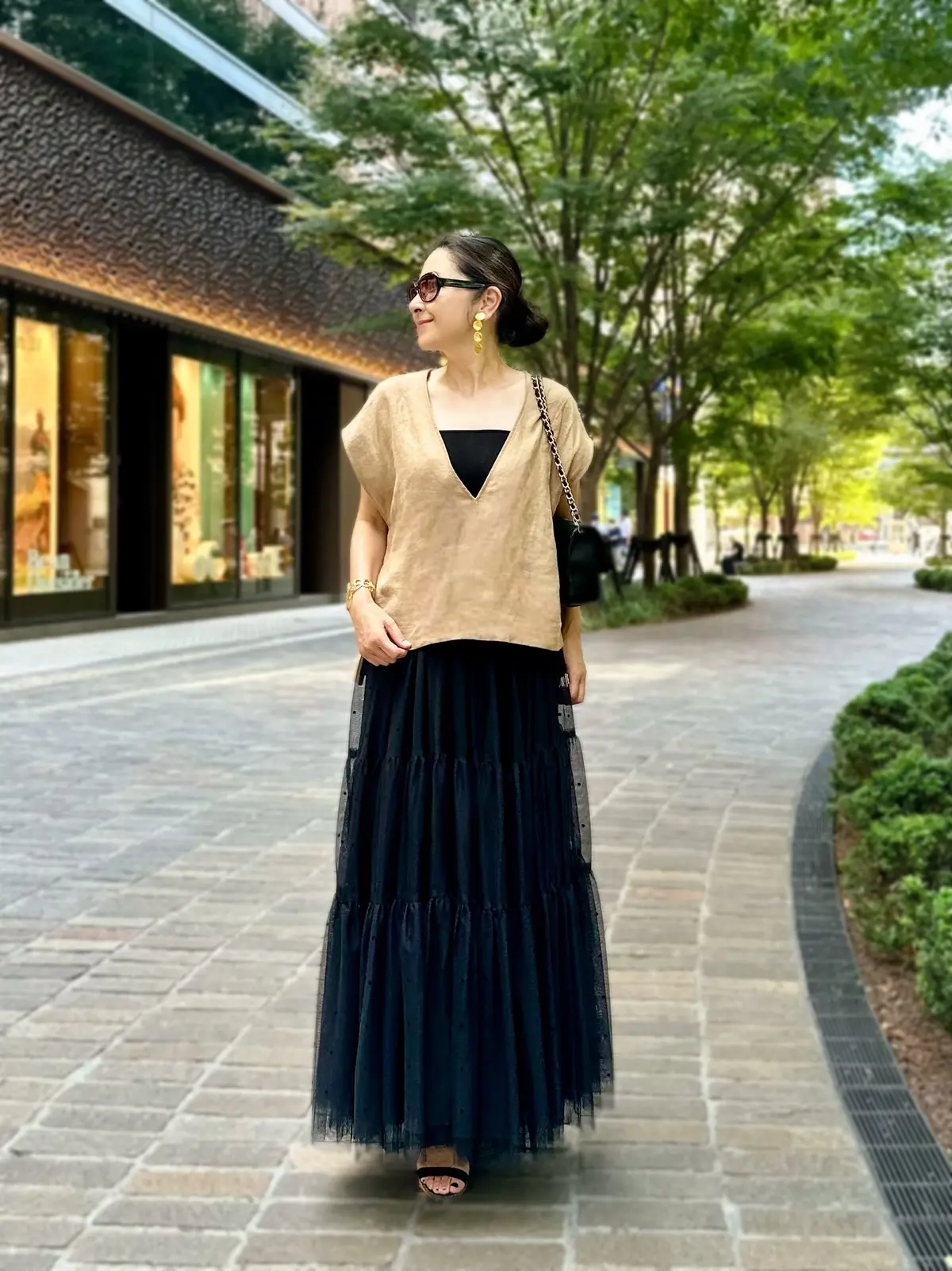 エクラプレミアムのキャメル「リネンコンパクトジレ」、黒のチュールスカート、黒のチェーンバッグ、黒のサンダル