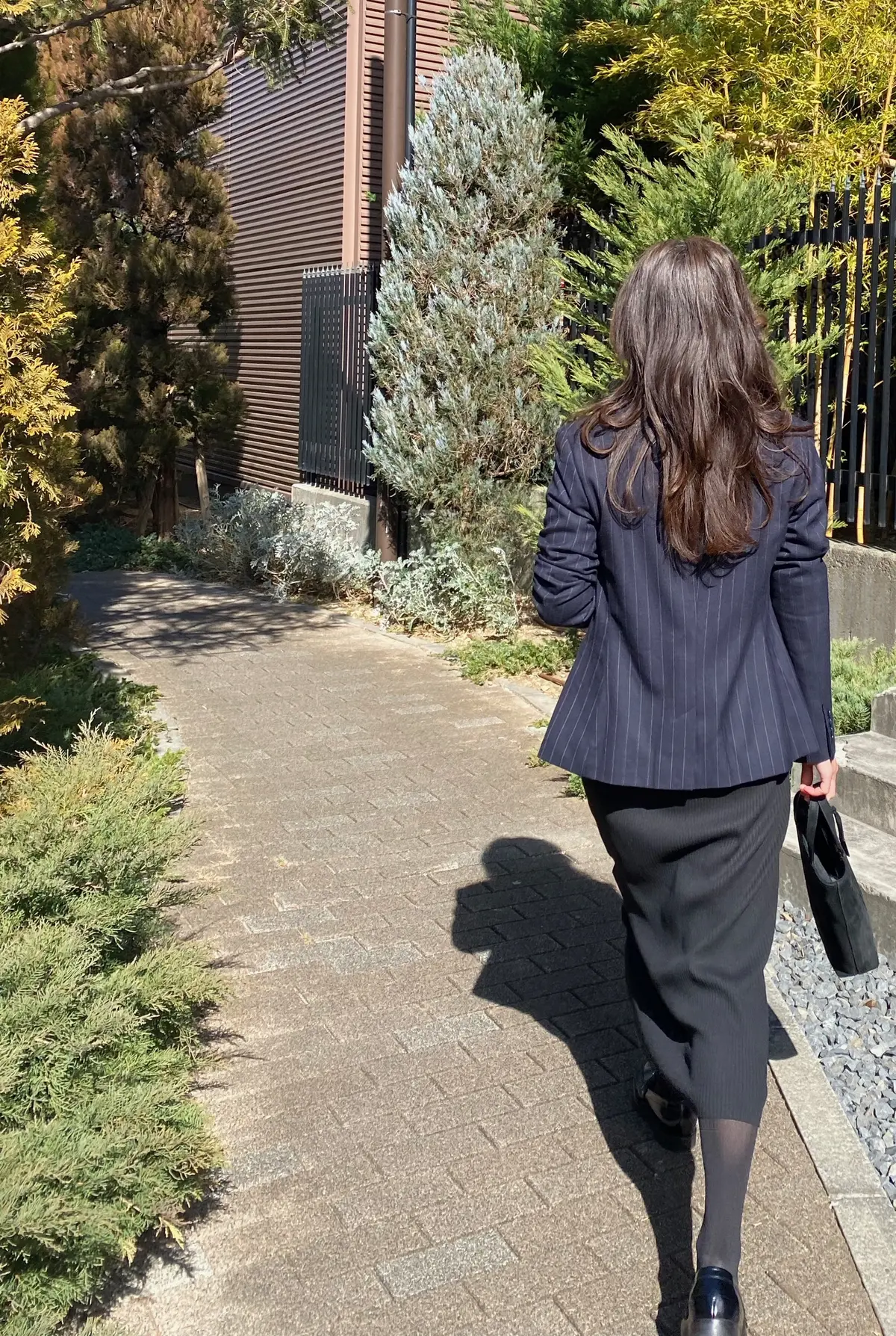 黒のユニクロハーフジップニットワンピースを着てローレンラルフローレンのジャケットを羽織りグッチのバッグを持ち歩くロングヘアの女性の後ろ姿