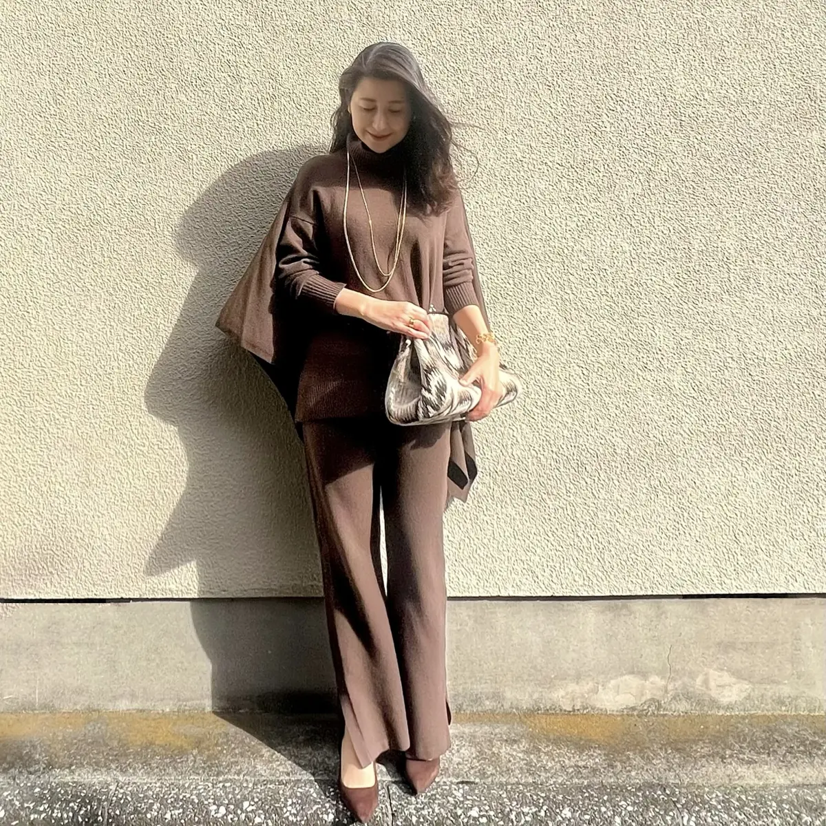 茶ニットパンツ、茶ポンチョニット、茶パンプス、大きめ柄物クラッチバッグ