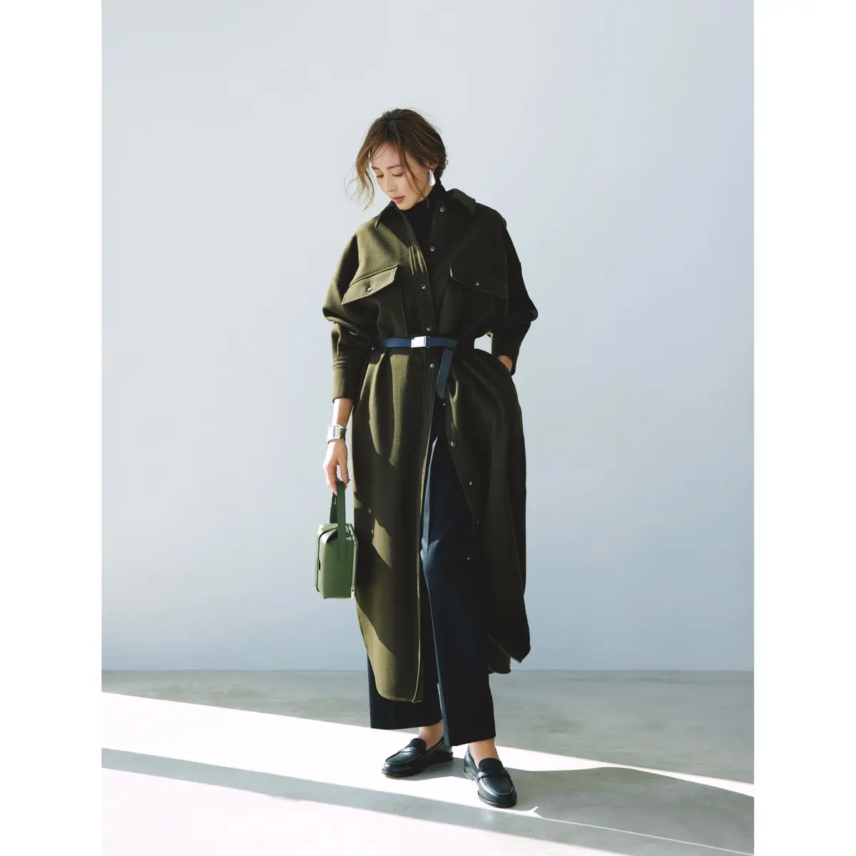 黒トップスと黒パンツの上からカーキのロング丈シャツを羽織ってベルトを締めたコーディネート　モデル・SHIHO
