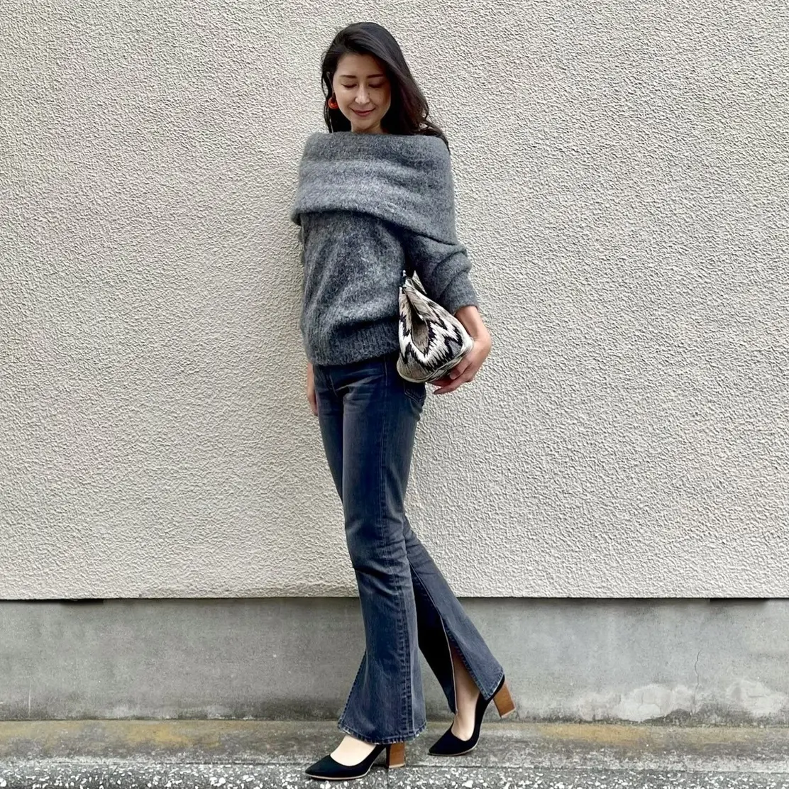 グレーのオフタートルニット、ブラックデニム、ブラックのパンプス、大きめのクラッチバッグ、オレンジのイヤリング