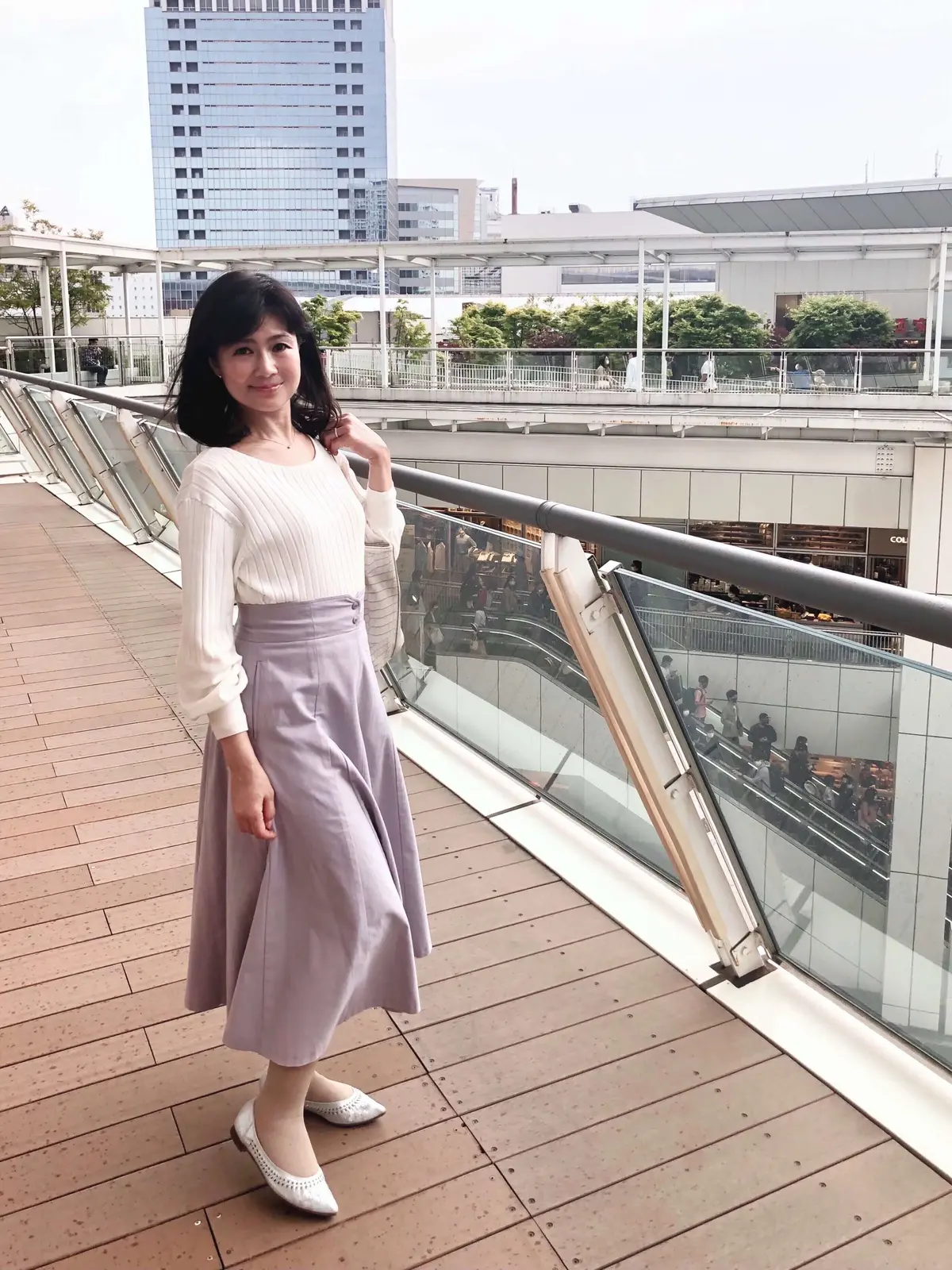 白のトップスに薄紫のロングスカート。シルバーのパンプス。