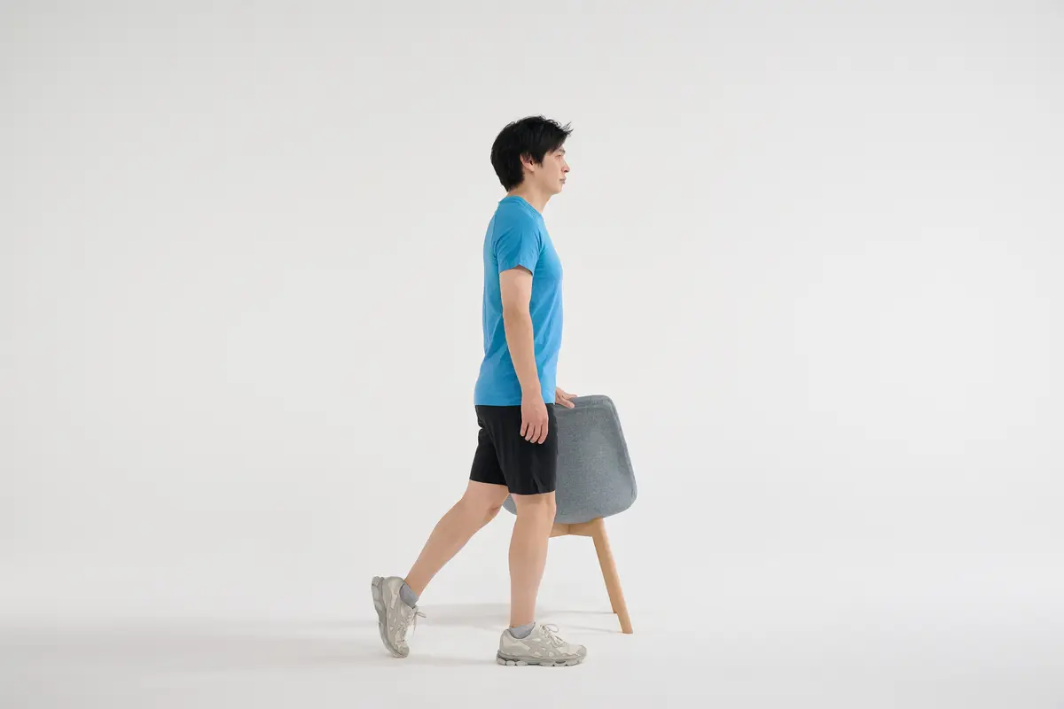 ① 椅子の右側に立ち、左手を椅子の背に置いて体を支え、左脚を後ろに引く。右足の膝のお皿とつま先はまっすぐ前に向ける。