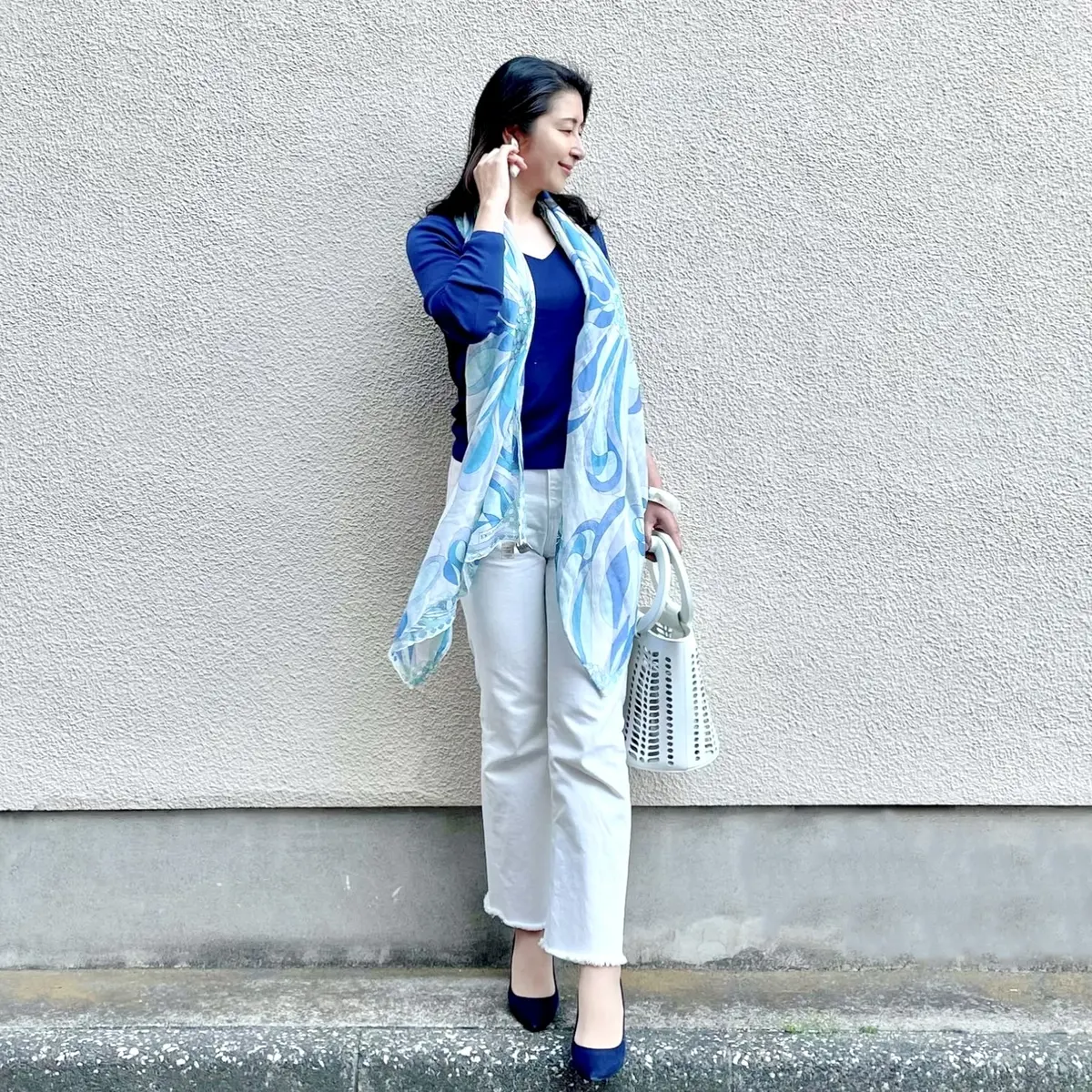 ホワイトデニム、ネイビーVネックニット、ネイビーパンプス、ブルー系大判ストール、白のバッグのコーディネート