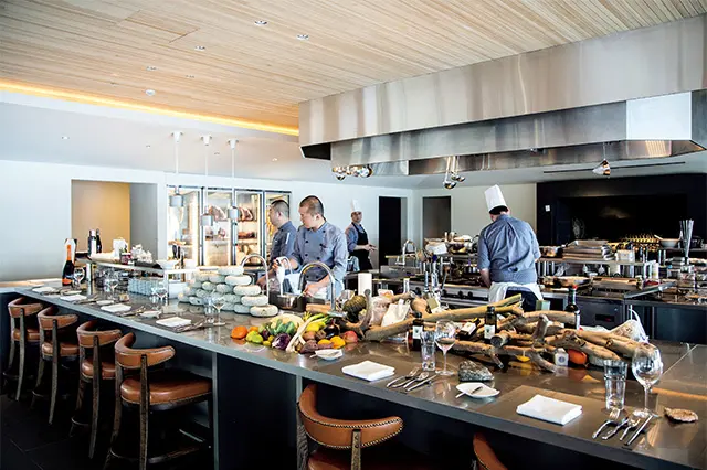 キッ チン内の臨場感を楽しめるシェフズテーブルのような大テーブル。ほかにプ ールに面したガラス張りのダイニングがある