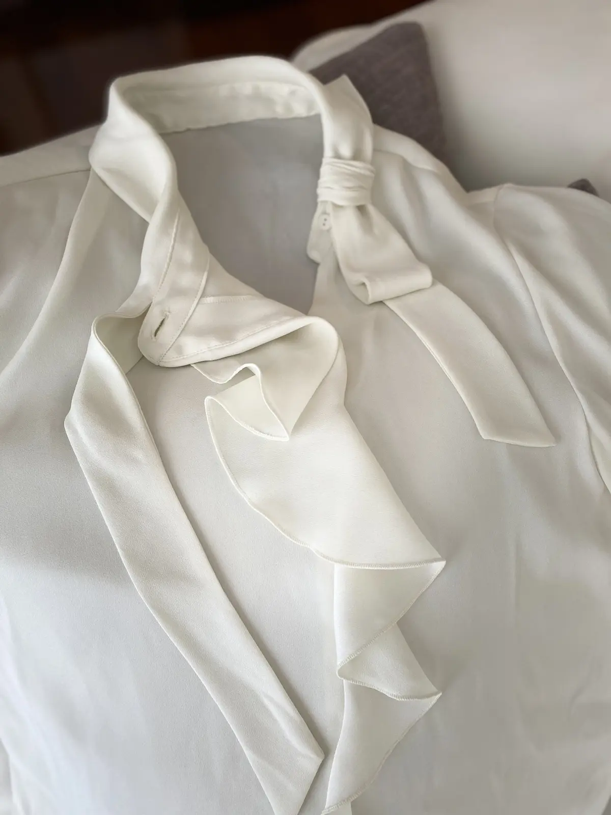 平置きしたストロベリーフィールズの巻かないボウタイブラウスをクローズアップ。首元から流れる立体フリルと、結ばずに固定されたボウタイデザインが分かるアップ画像（シルクライク素材の艶感も）。