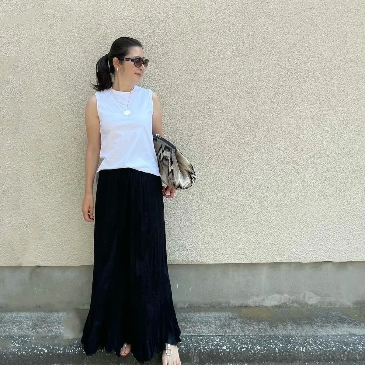 ユニクロの白ノースリーブTシャツ、黒のマキシ丈スカート、大きめのクラッチバッグ、シルバーのフラットサンダル、パールとシルバーの細めネックレス