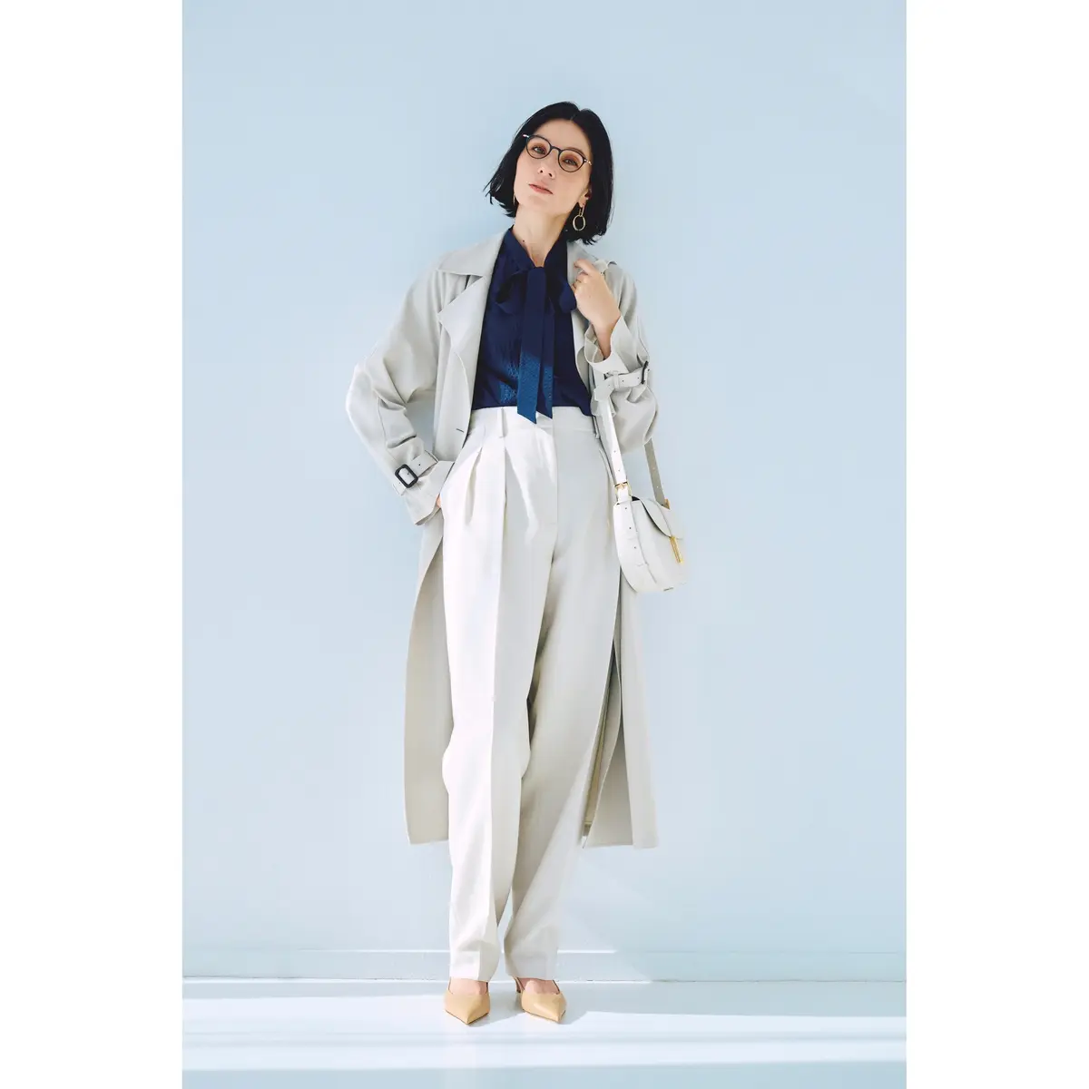 白のタックパンツとネイビーボウタイブラウスのコーデにライトベージュのトレンチコートを羽織った着こなし　モデル・田沢美亜