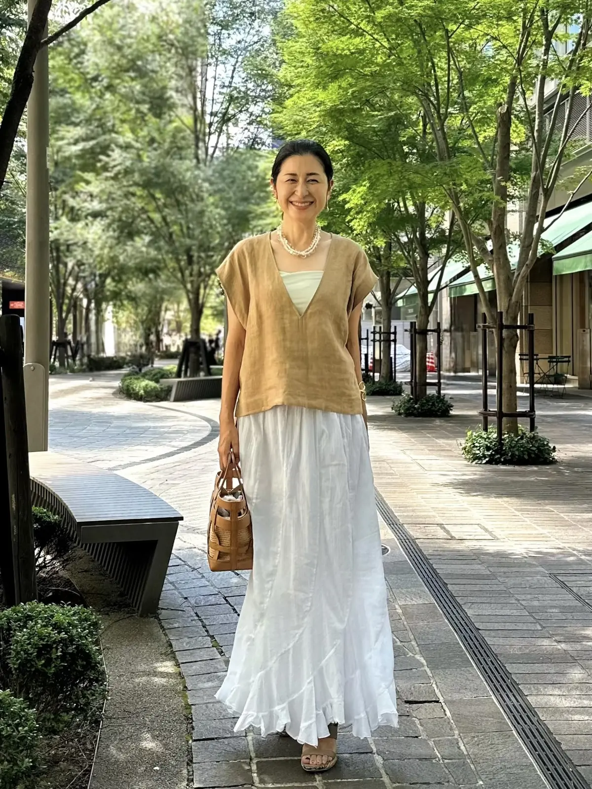 エクラプレミアムのキャメル「リネンコンパクトジレ」、白のロングスカート、キャメルのバッグ、ベージュのサンダル