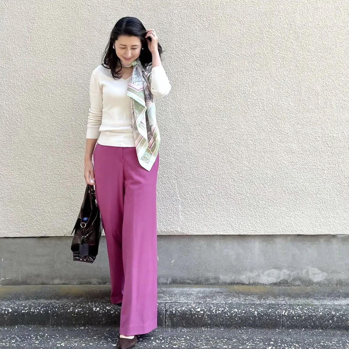 白のVネックニット、ピンクのワイドパンツ、スカーフ、ブラウンのバッグとパンプス