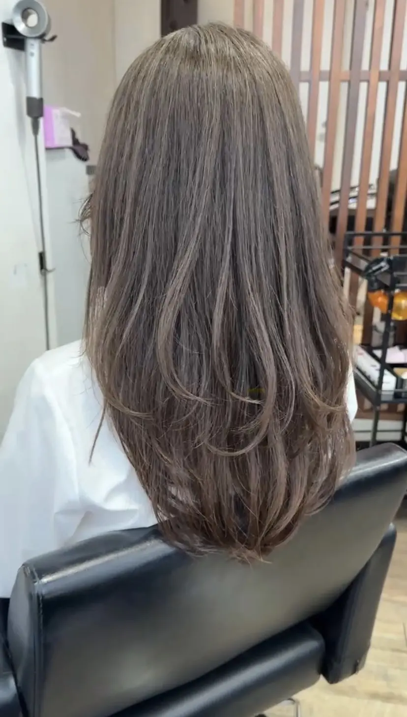 原宿「ハーツ」店内の椅子に座るロングヘア女性。ナチュラルなレイヤーで動きが出たロングの後ろ姿。透明感のあるベージュカラーがツヤ感を引き立て、上品な仕上がりに。