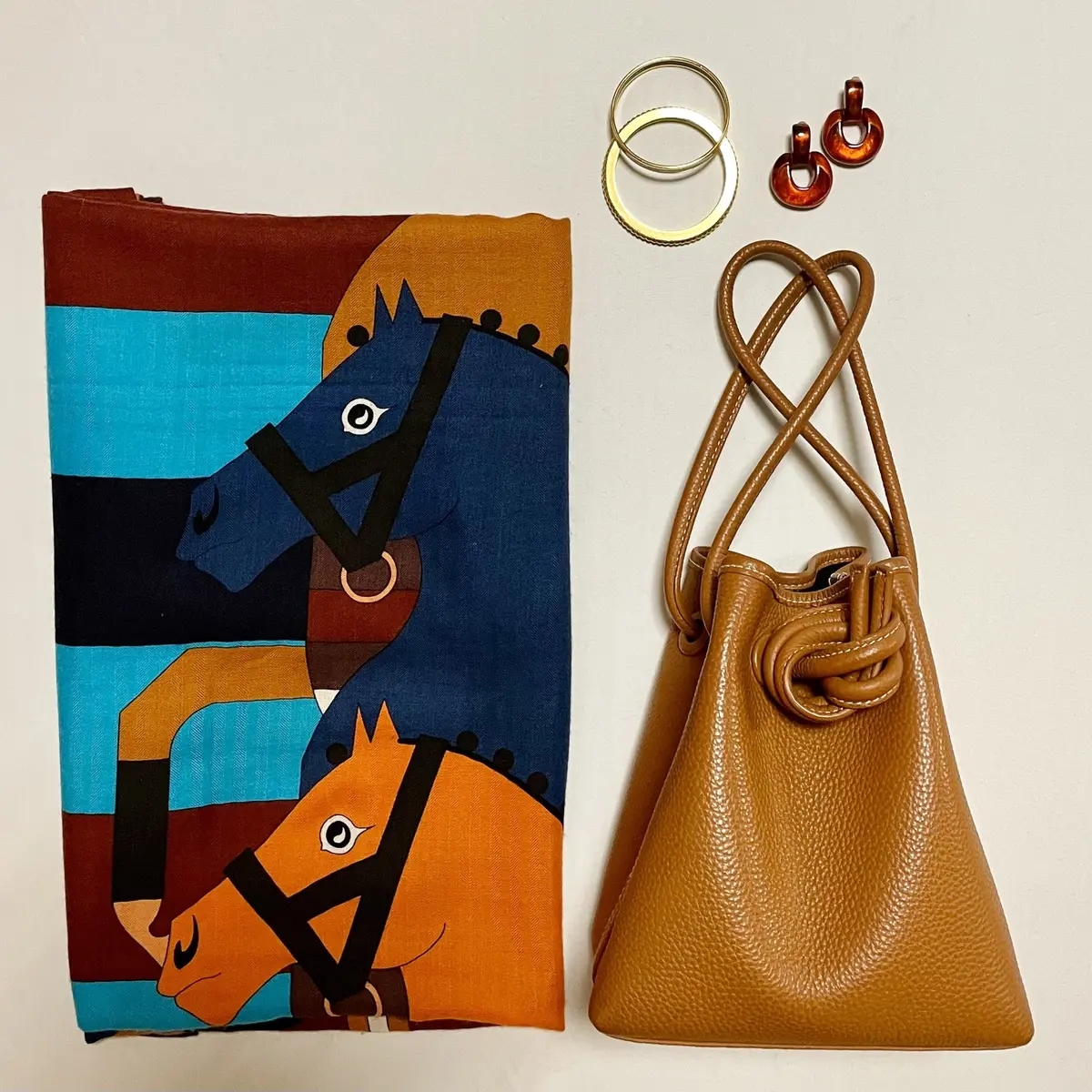 スカーフ柄の大きめストール、キャメルのバッグ、ゴールドの細めバングル、オレンジのイヤリング