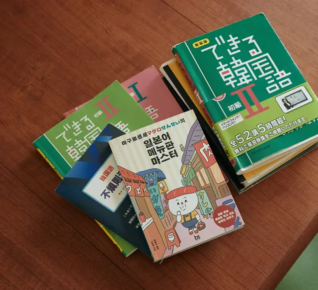 メインで使っているのは『できる韓国語』シリーズ（アスク出版）。現在は「初級Ⅱ」を学んでいる。イラストが表紙の本は、韓国語の先生に初めて会ったときにもらった『マグロせんせいの日本語メニューマスター』。