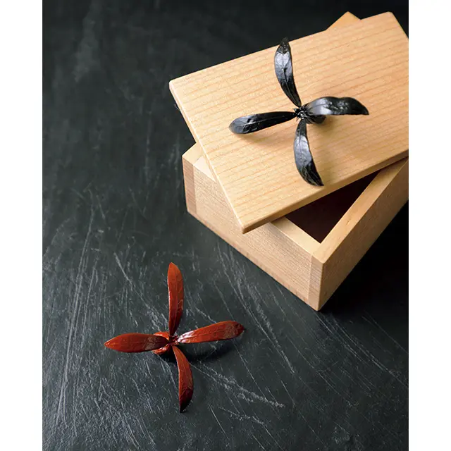 邪気をはね（羽根）のけ、厄除けと成長を願い、古く は、女の子が初めて正月を迎える際に贈られた羽子板。 羽子板を思わせる台形の木箱に漆塗りのツクバネの実 を納めた羽子板のしつらい￥16,500