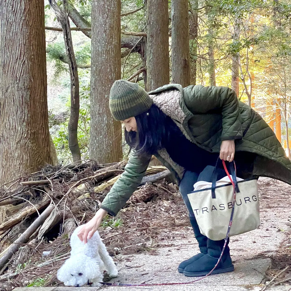 カーキのキルティングコート、ブラックデニム、ブラックのムートンブーツ、エクラ10月号の付録バッグ、グリーン系のニット帽、白のトイプードル犬